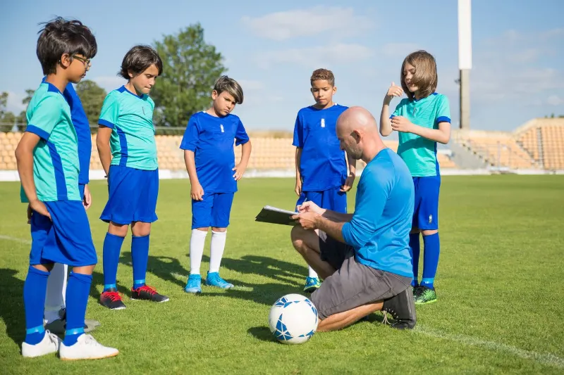 Futbol sahasında çocuklara taktik anlatan antrenör