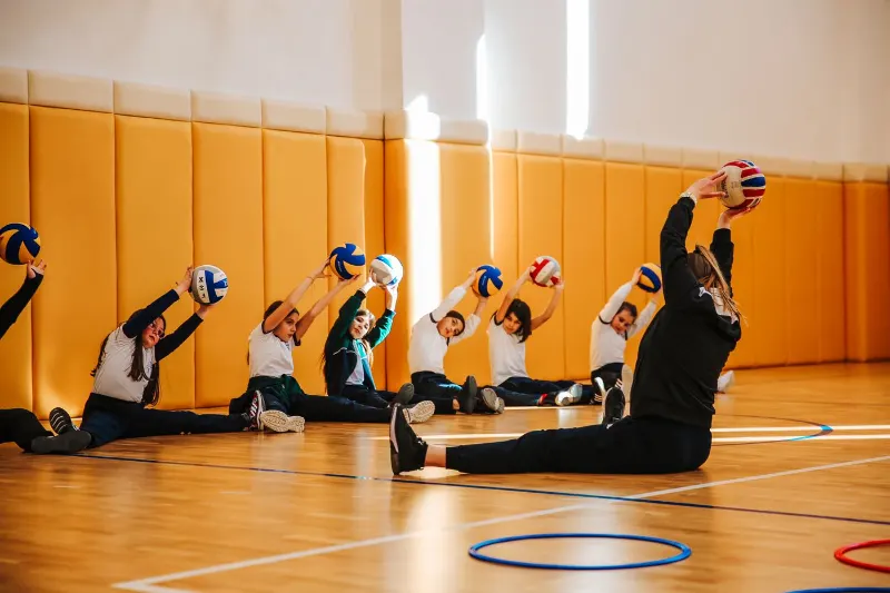 Spor salonunda voleybol toplarıyla esneme çalışması yapan öğrenciler